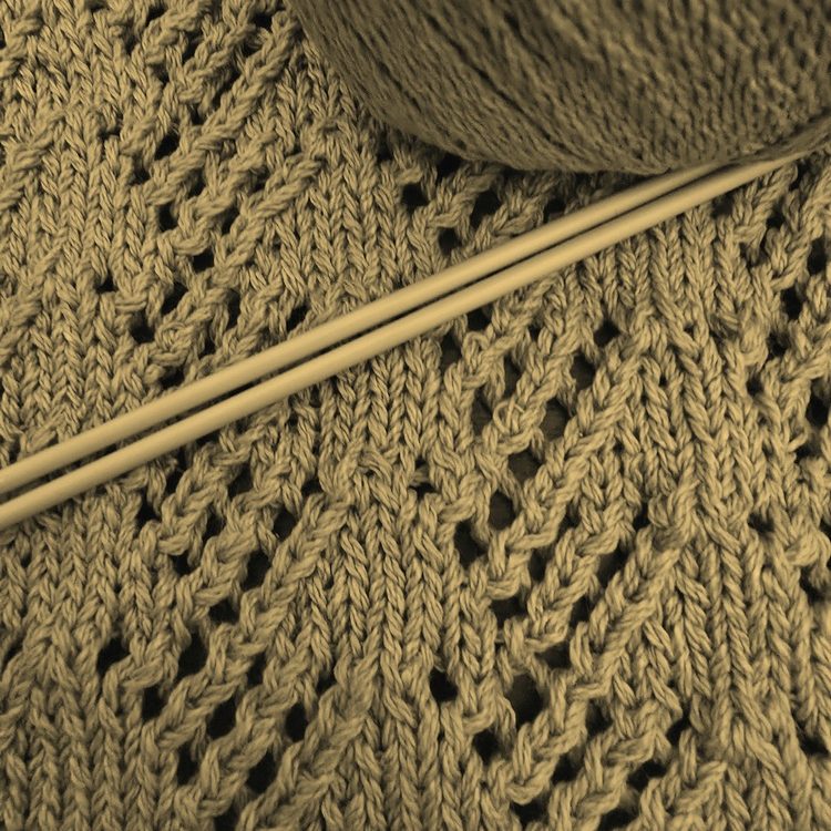 Knitted fabric in a delicate pattern with a ball of yarn and knitting needles.